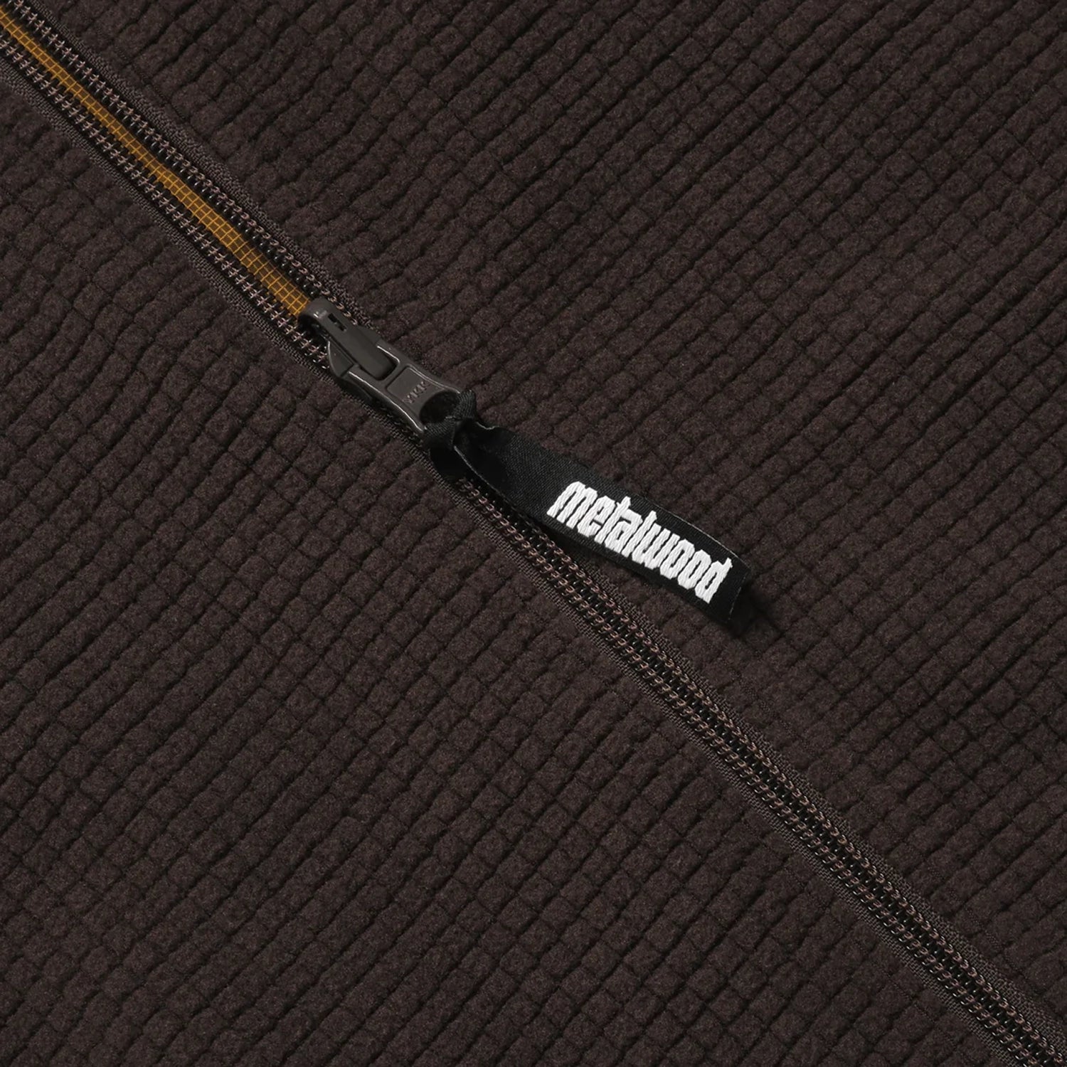 Close-up of a textured brown dijon vest with a zipper and 'Metalwood' brand logo.