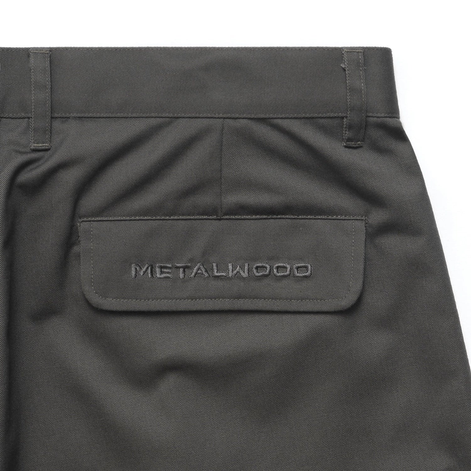 Close up of Olive Metalwood Studio Trophy Shorts with a brand label the back pocket on a white background