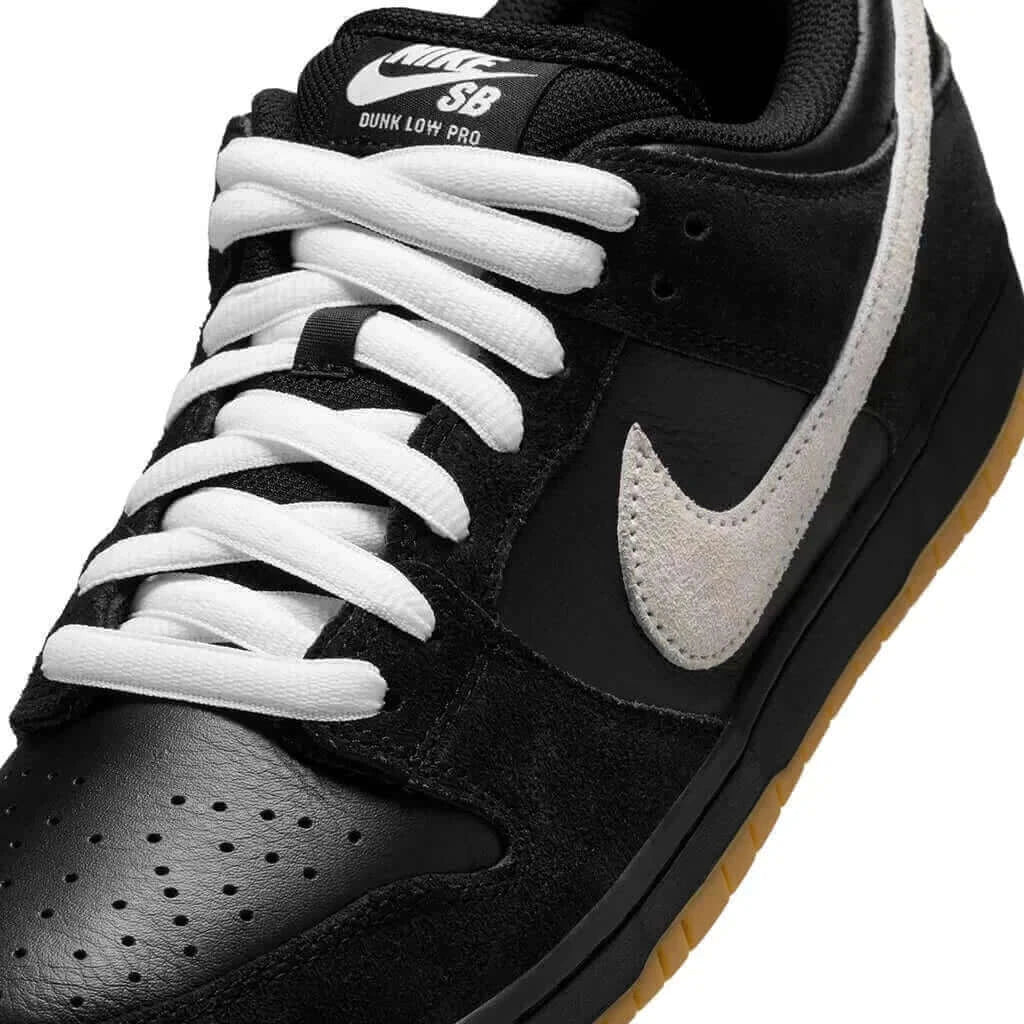 A close up of Nike SB Dunk Low Pro shoe featuring a black and white color scheme with a tan sole on white background.