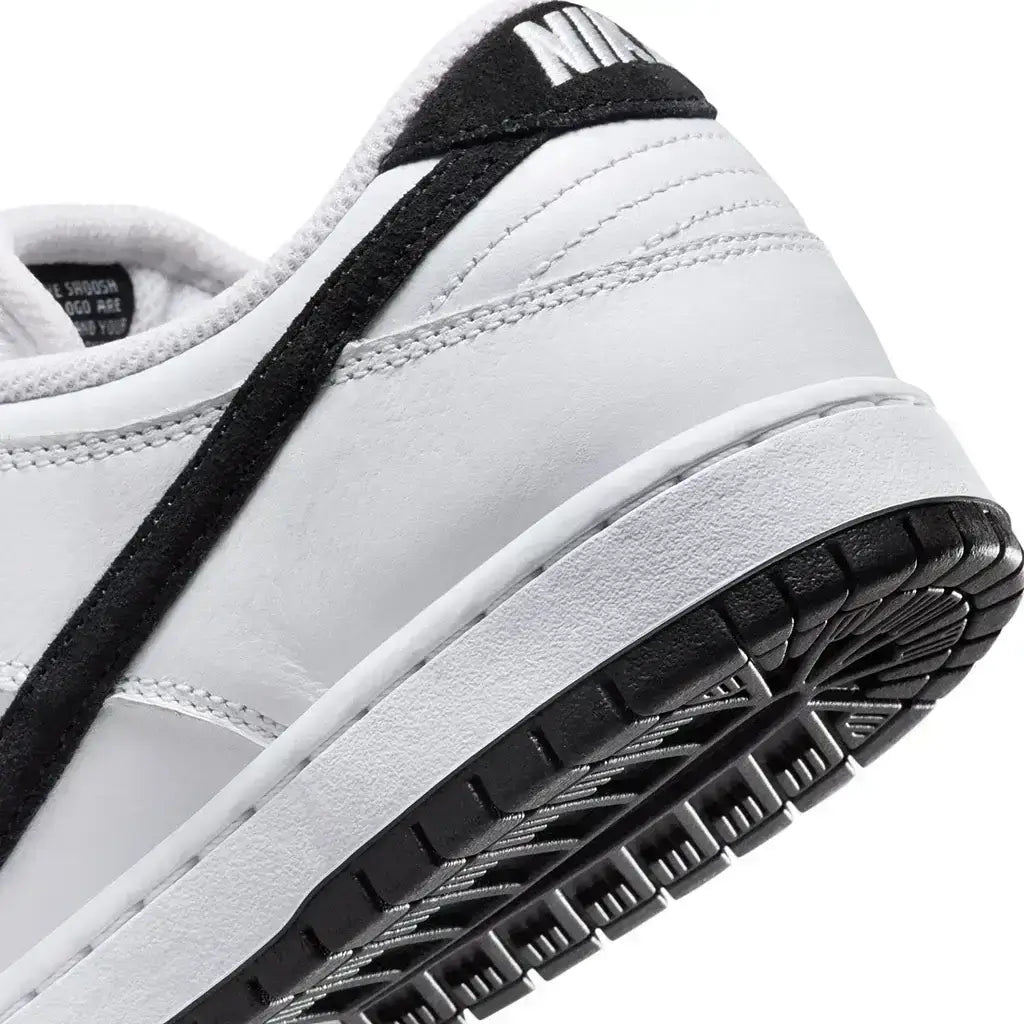 A close up of the heel of a Nike SB Dunk Low Pro shoe featuring white uppers with black accents and a black outsole on a white background.