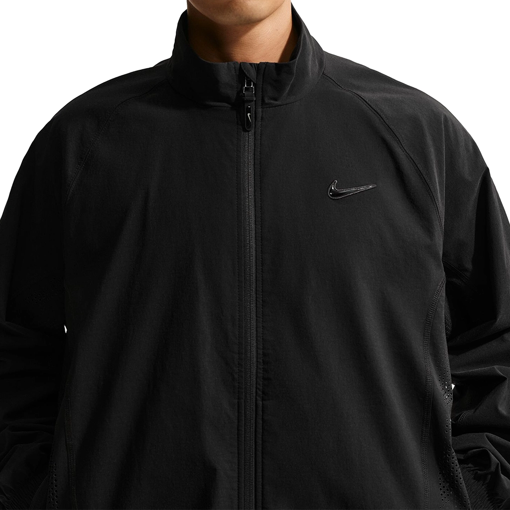Close up of a person wearing a black Nike SB Ishod Wair track jacket with a Nike logo on a white background