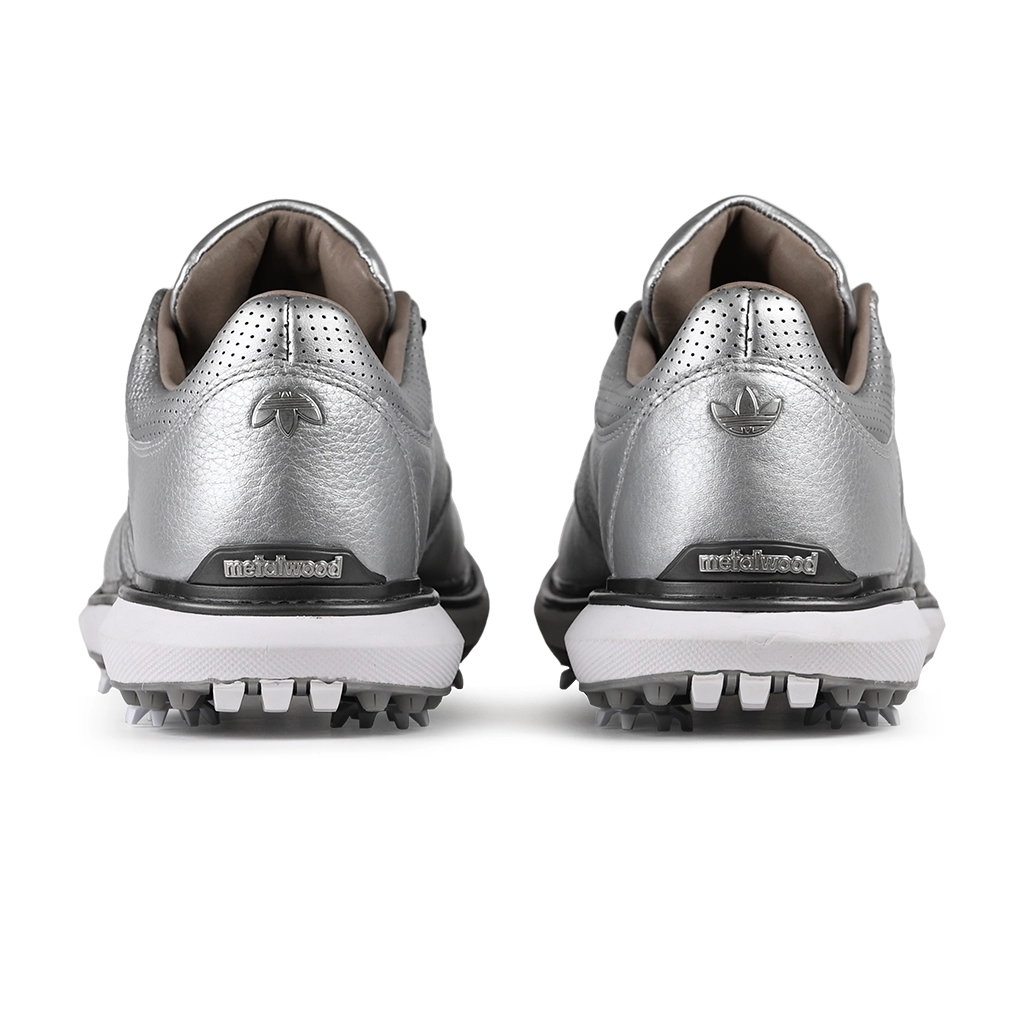 A close up of silver metallic Adidas x Metalwood MC70 golf shoe with co-branding on the heel on a white background