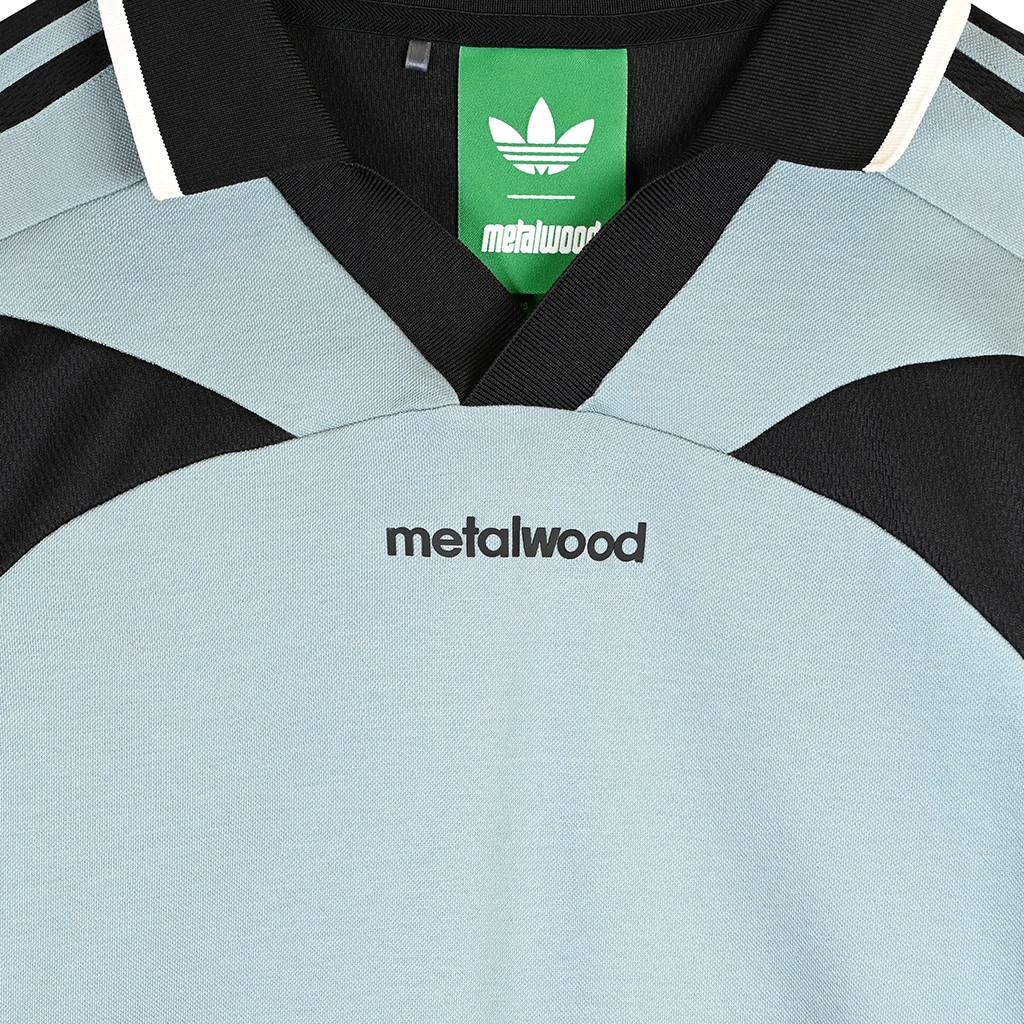 Close up of Green Earth Adidas x Metalwood Studio golf polo with black accents on a white background