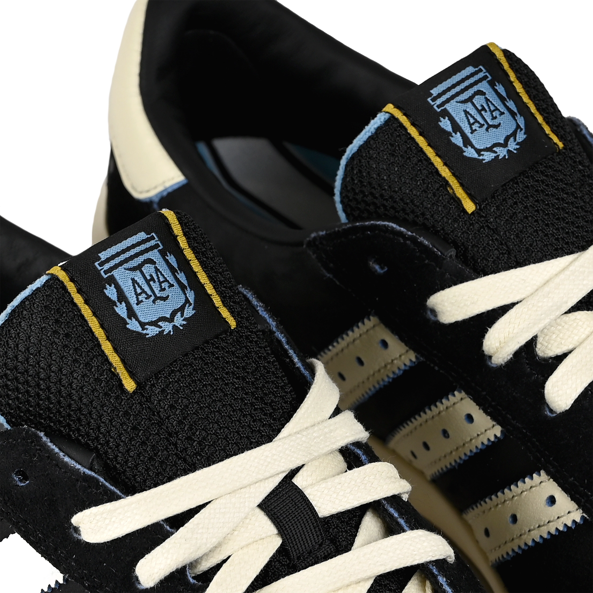 Tongue tags of Core black and cream white adidas Skateboarding x Thrasher Magazine x Argentina Football Association Glenburn skateboard sneaker with AFA logo on a white background