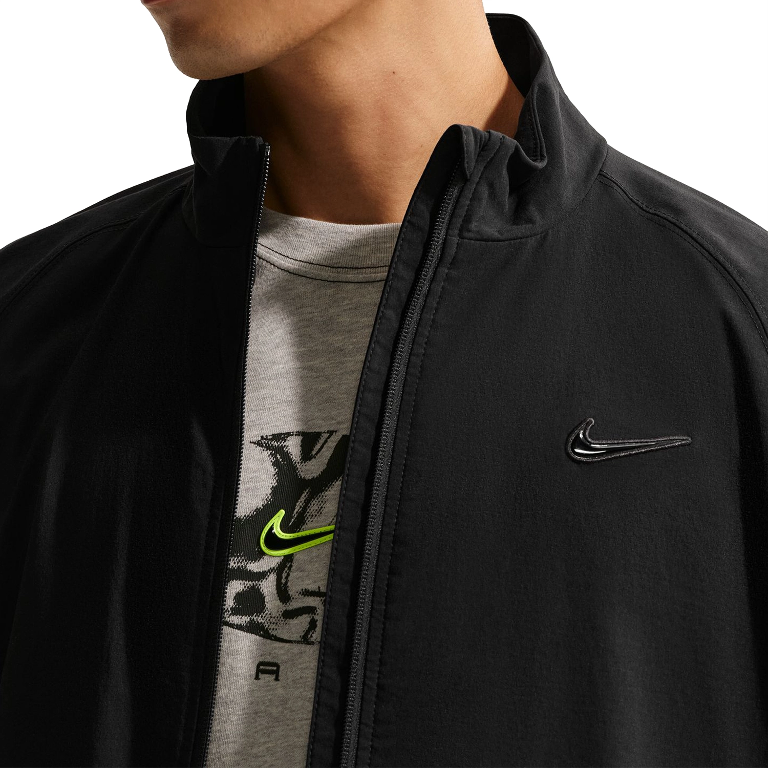 Close up of person wearing a black Nike SB Ishod Wair track jacket over a gray t-shirt with a Nike logo on a white background