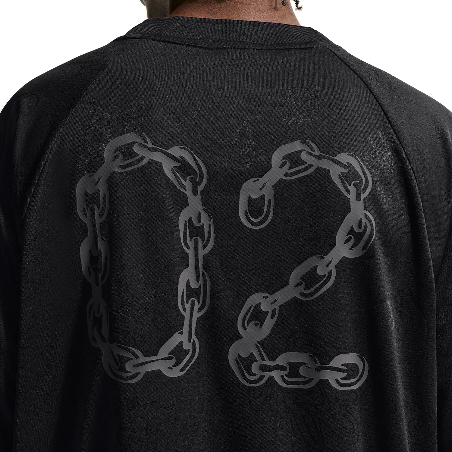 Close up of person wearing a black Nike SB Jacquard Skate Jersey with chain graphic on a white background
