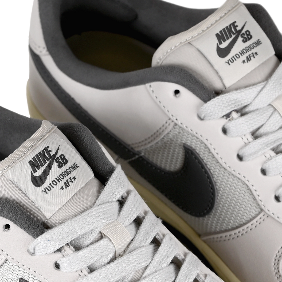Tongue tags of White leather and mesh Nike SB x Yuto Horigome Air Force 1 skateboard sneakers with iron grey swoosh and family crest on a white background