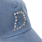 Close up of Blue Dime MTL Waxed Worker baseball cap with decorative studs on a white background