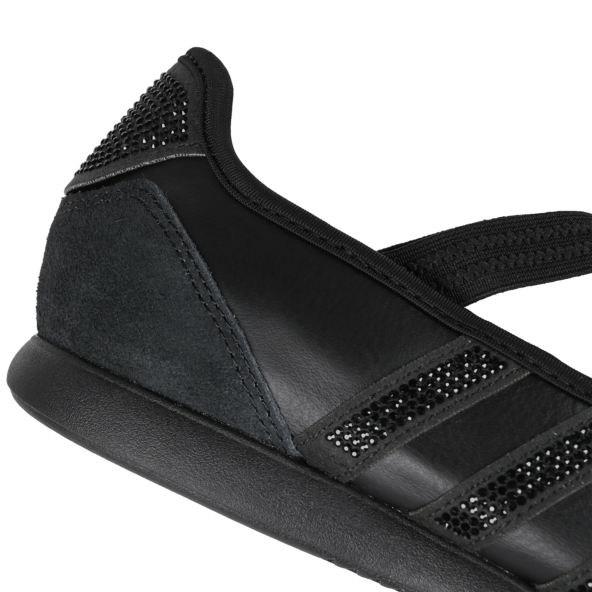 Close up of core black Adidas Originals Mary Jane sneaker with textured leather and suede panels, three rhinestone-embellished stripes, and a black elastic strap across the instep on a white background.