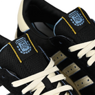 Tongue tags of Core black and cream white adidas Skateboarding x Thrasher Magazine x Argentina Football Association Glenburn skateboard sneaker with AFA logo on a white background