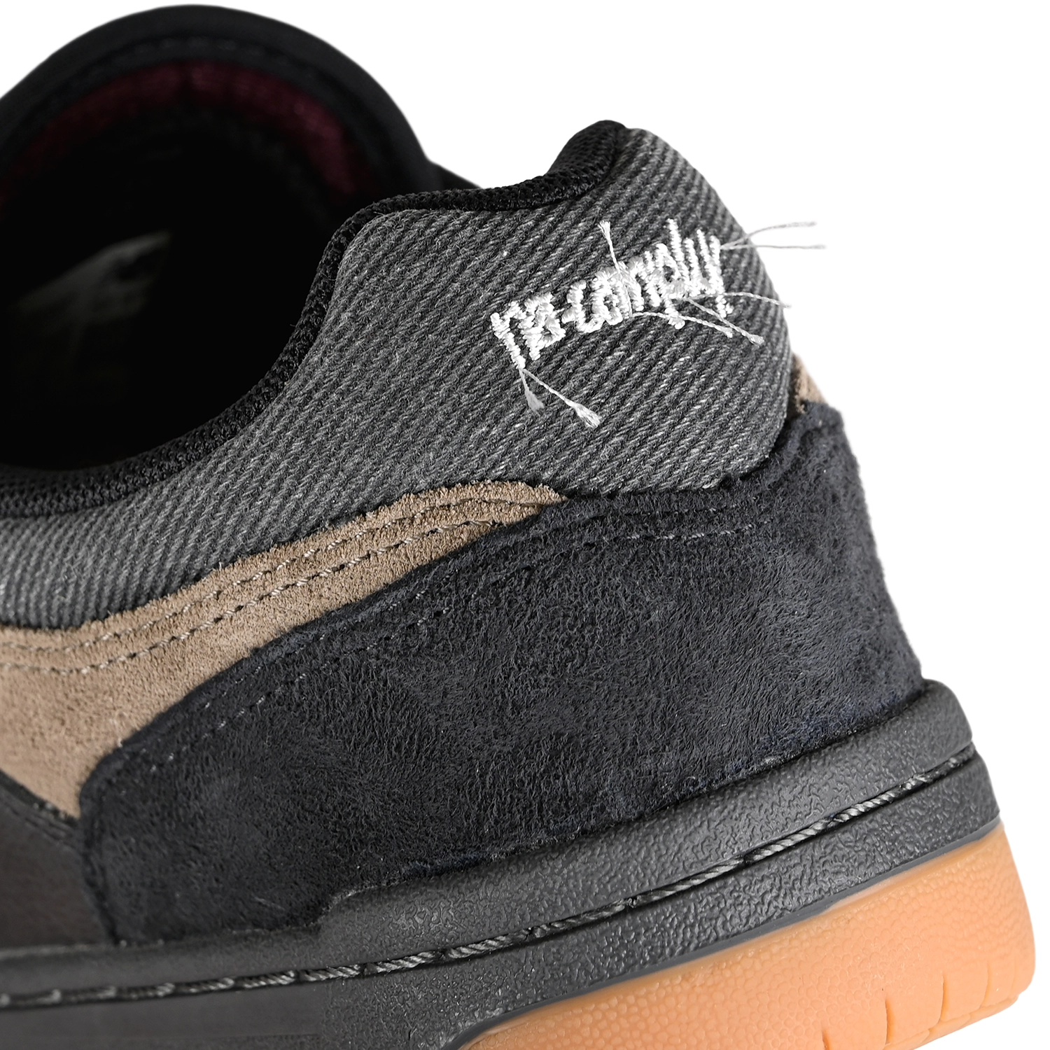 Close up of Black and arid stone New Balance Numeric x No-Comply NM480 skateboard sneaker with frayed Script logo embroidered on denim heel collar on a white background